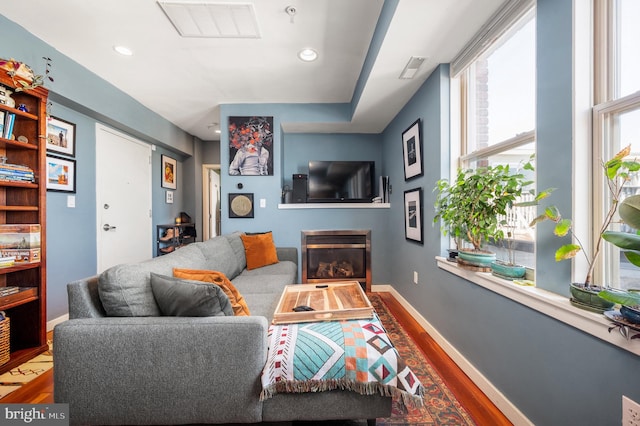 living area featuring wood finished floors, a glass covered fireplace, baseboards, and recessed lighting