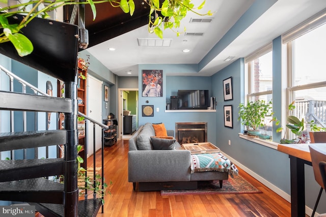 living room featuring wood-type flooring, baseboards, a glass covered fireplace, and recessed lighting