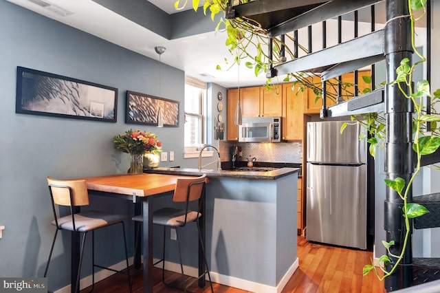 kitchen with appliances with stainless steel finishes, light wood-style flooring, tasteful backsplash, a peninsula, and baseboards