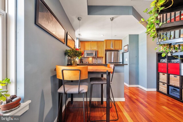 kitchen with stainless steel appliances, backsplash, light wood finished floors, baseboards, and a kitchen breakfast bar