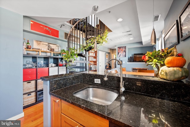 kitchen featuring a sink, light wood-type flooring, hanging light fixtures, open floor plan, and dark stone counters