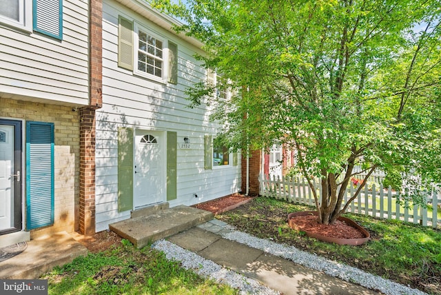 doorway to property featuring fence and brick siding