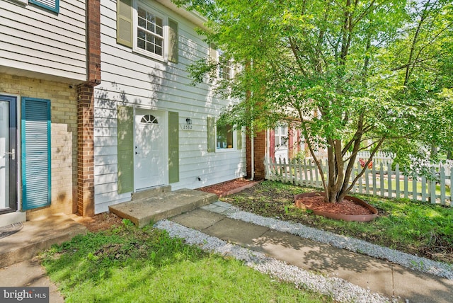 doorway to property featuring fence and brick siding