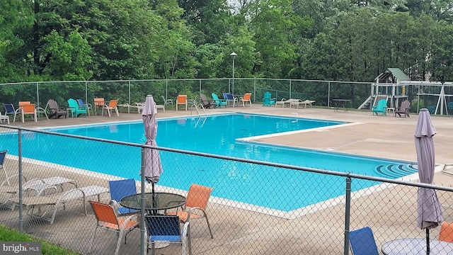 community pool featuring fence, a patio area, and a view of trees
