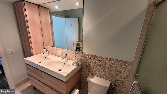 bathroom featuring toilet, tile walls, wainscoting, double vanity, and tile patterned flooring