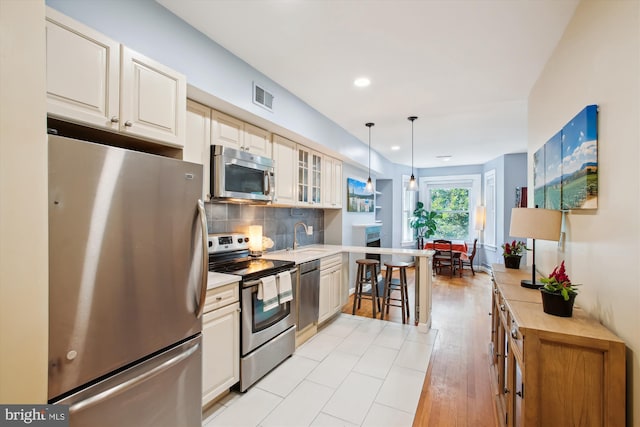 1725 Willard St NW Unit 3, Washington, DC 20009 - kitchen featuring appliances with stainless steel finishes, light countertops, glass insert cabinets, backsplash, and decorative light fixtures