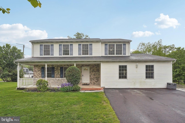 view of front of house featuring covered porch, a front yard, brick siding, and driveway