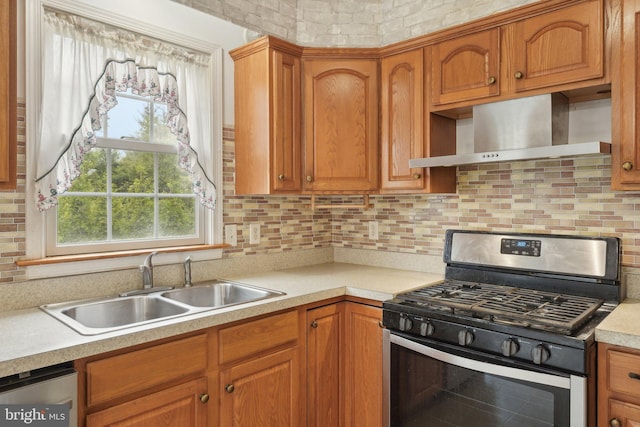 kitchen featuring appliances with stainless steel finishes, wall chimney range hood, a sink, light countertops, and healthy amount of natural light
