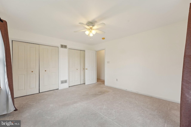 unfurnished bedroom featuring multiple closets, light carpet, baseboards, and a ceiling fan