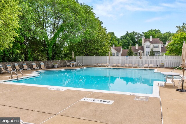 community pool with a patio area, fence, and view of scattered trees