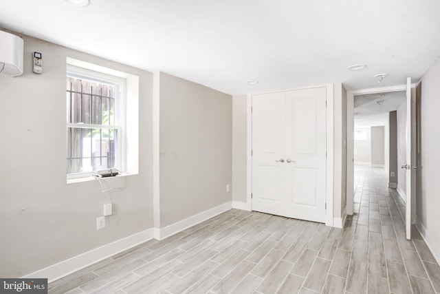 empty room featuring baseboards, light wood-type flooring, a wall mounted AC, and recessed lighting