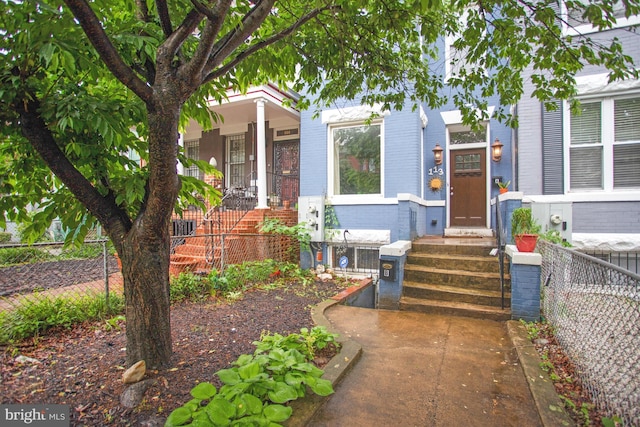 view of front of home with brick siding, fence, entry steps, and a porch