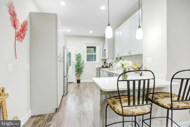 kitchen featuring gas stove, light wood-type flooring, baseboards, white cabinets, and a peninsula