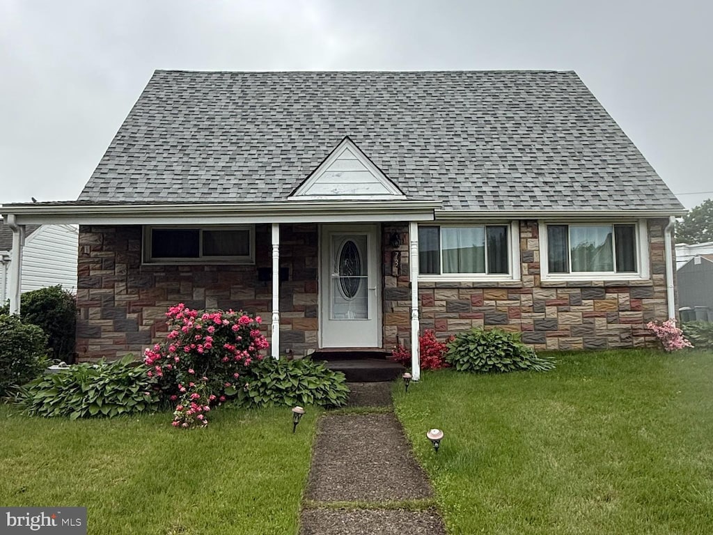 bungalow-style house with roof with shingles, a front yard, and stone siding