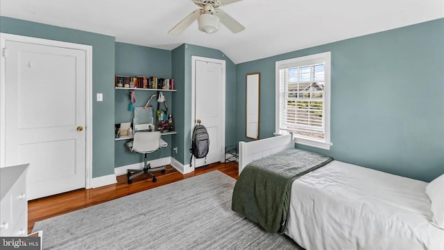 bedroom featuring wood finished floors, vaulted ceiling, an office area, a ceiling fan, and baseboards