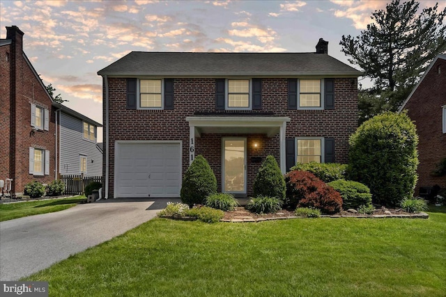 colonial house with a front lawn, a garage, brick siding, and asphalt driveway