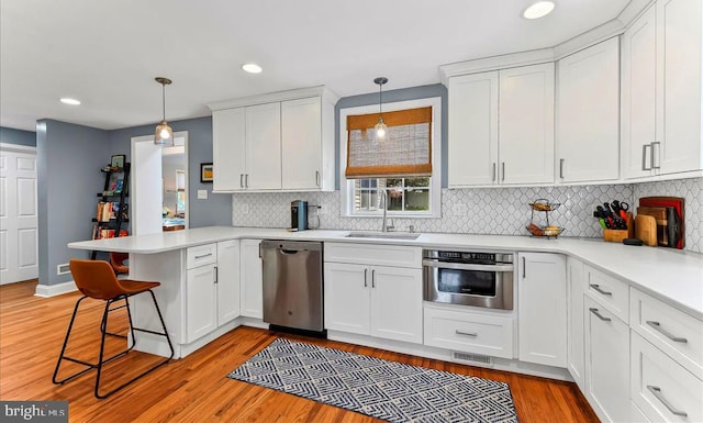 kitchen with stainless steel appliances, a sink, a peninsula, white cabinets, and backsplash
