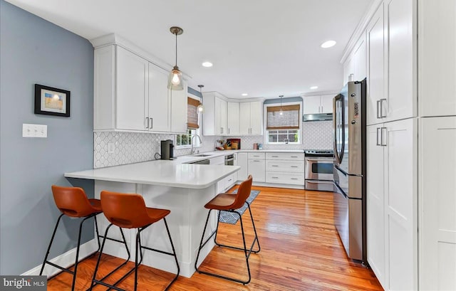 kitchen featuring appliances with stainless steel finishes, under cabinet range hood, a peninsula, a breakfast bar area, and tasteful backsplash