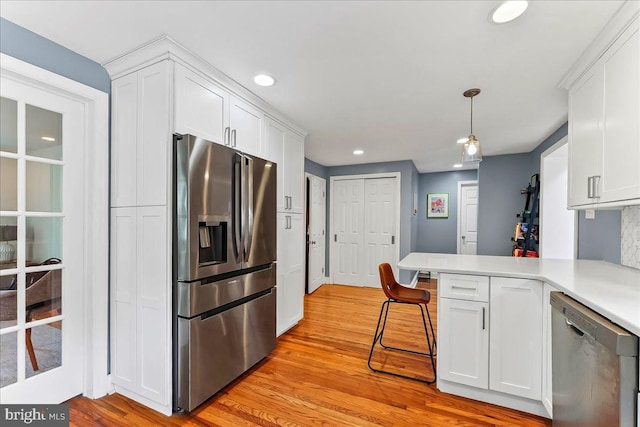 kitchen featuring appliances with stainless steel finishes, light wood finished floors, white cabinetry, recessed lighting, and a peninsula