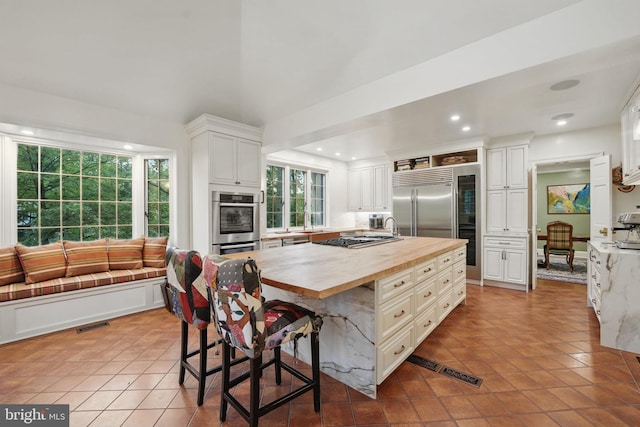 4301 Forest Ln NW, Washington, DC 20007 - kitchen featuring butcher block counters, stainless steel appliances, white cabinetry, tile patterned floors, and a kitchen island with sink