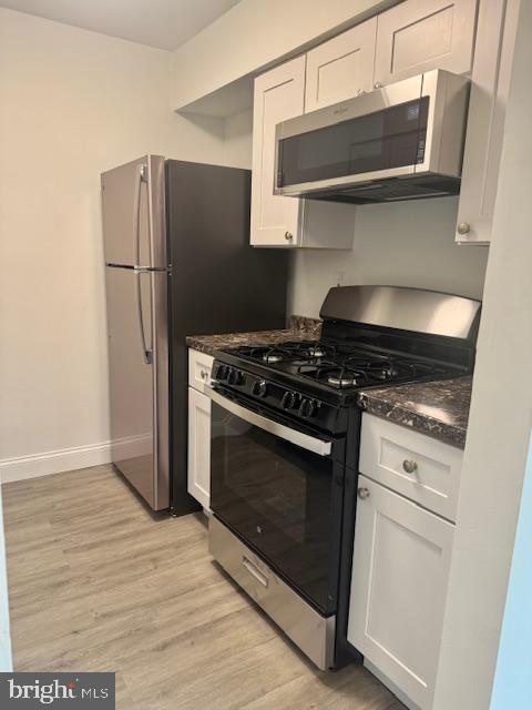 106 Mountain Rd Unit 2C, Glen Burnie, MD 21060 - kitchen with gas range oven, stainless steel microwave, dark countertops, light wood-style flooring, and white cabinets