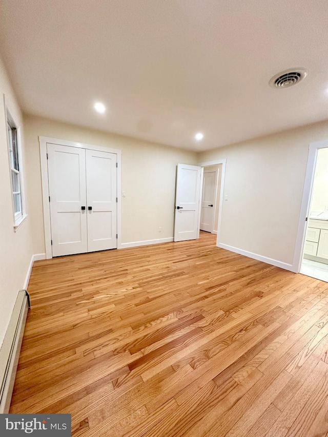 unfurnished bedroom featuring a baseboard radiator, light wood-type flooring, recessed lighting, baseboards, and connected bathroom