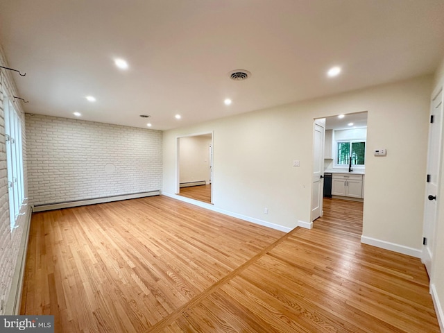 spare room featuring brick wall, light wood-style flooring, baseboard heating, baseboards, and recessed lighting