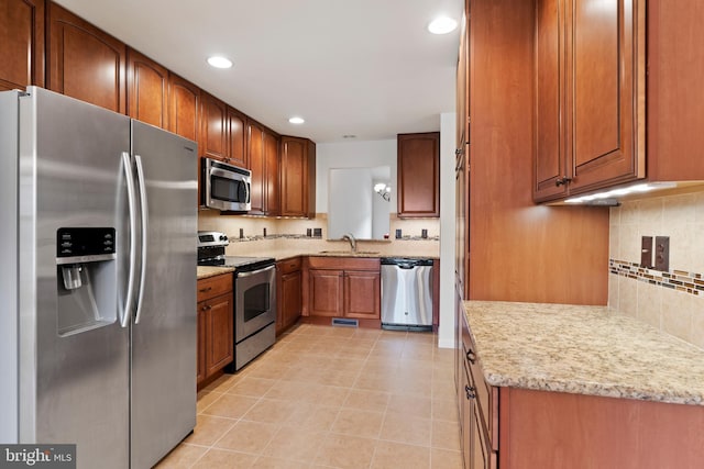 kitchen featuring appliances with stainless steel finishes, a sink, backsplash, recessed lighting, and brown cabinetry