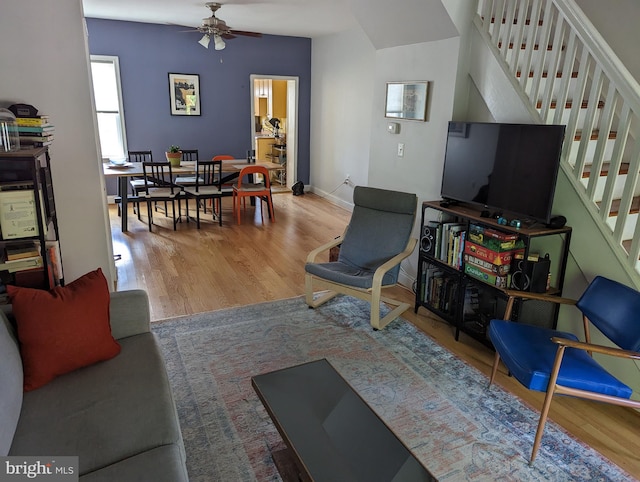 living room with wood finished floors, a ceiling fan, stairway, and baseboards
