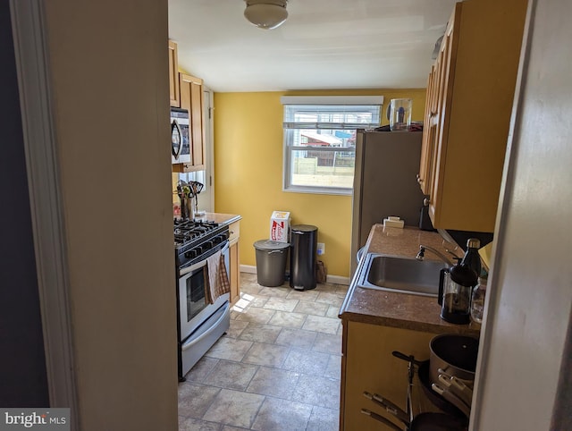 kitchen featuring appliances with stainless steel finishes, a sink, dark countertops, stone finish flooring, and baseboards