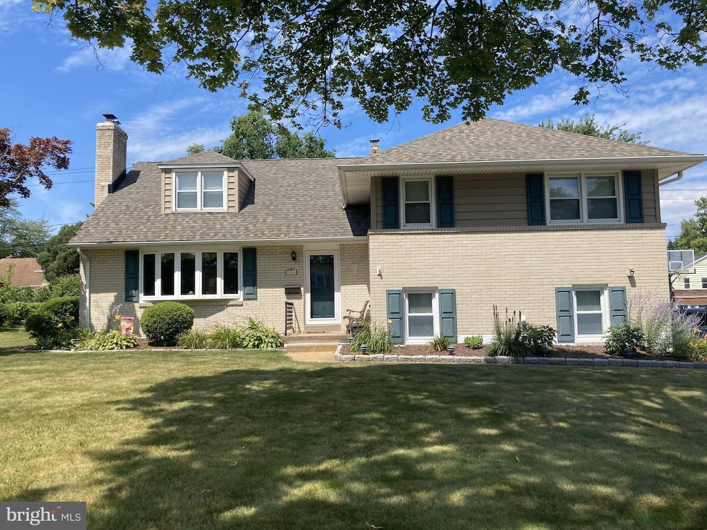 split level home featuring brick siding, a chimney, a front lawn, and a shingled roof