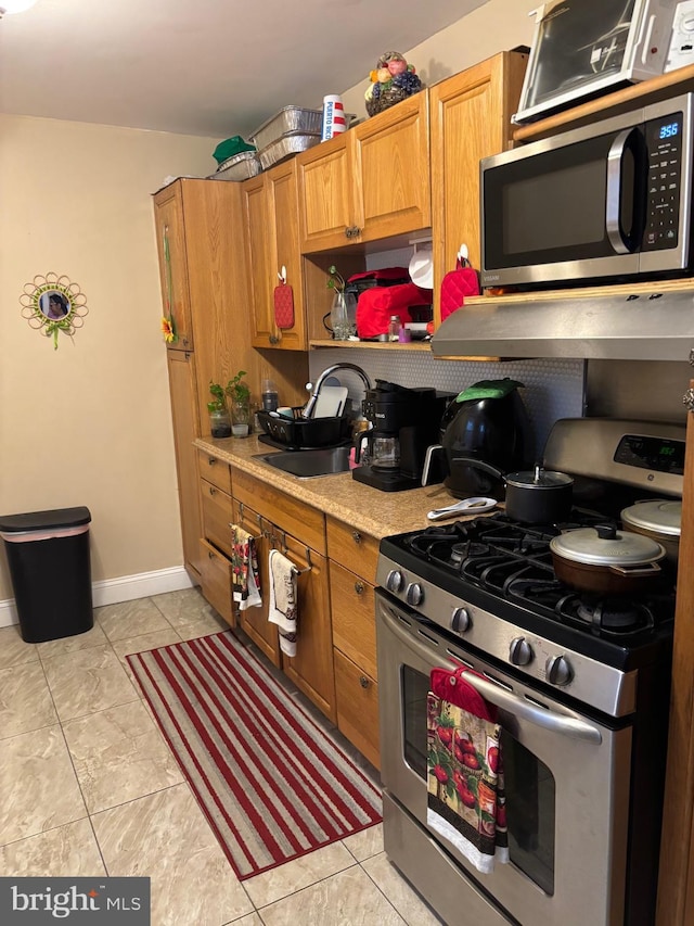 3737 N 5th St, Philadelphia, PA 19140 - kitchen featuring stainless steel appliances, a sink, light countertops, brown cabinetry, and wall chimney range hood