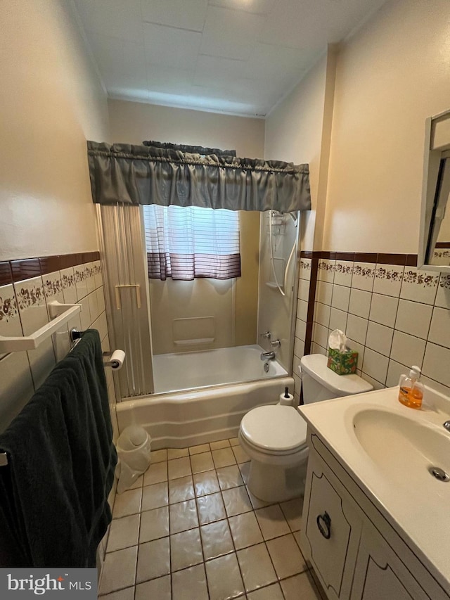 full bathroom featuring tile walls, wainscoting, tile patterned flooring, shower / bath combination, and toilet