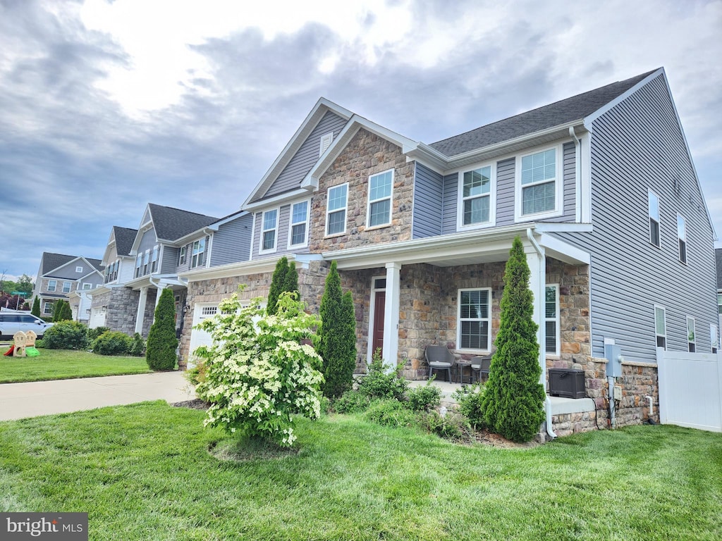 craftsman inspired home with stone siding, a front lawn, concrete driveway, a garage, and a residential view