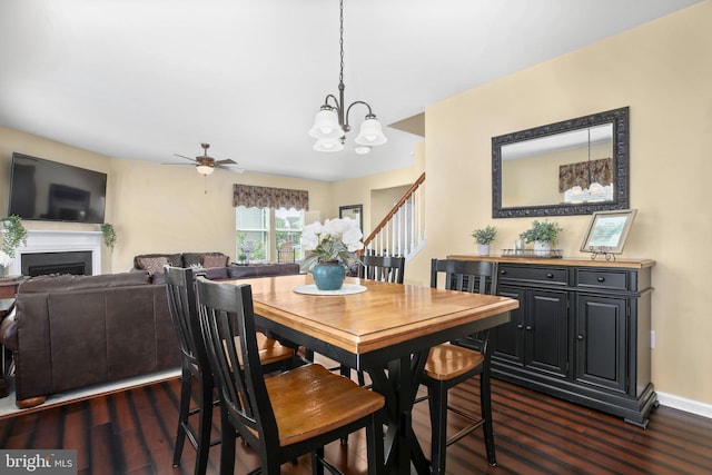 dining area featuring dark wood finished floors, a chandelier, a fireplace, ceiling fan, and stairway