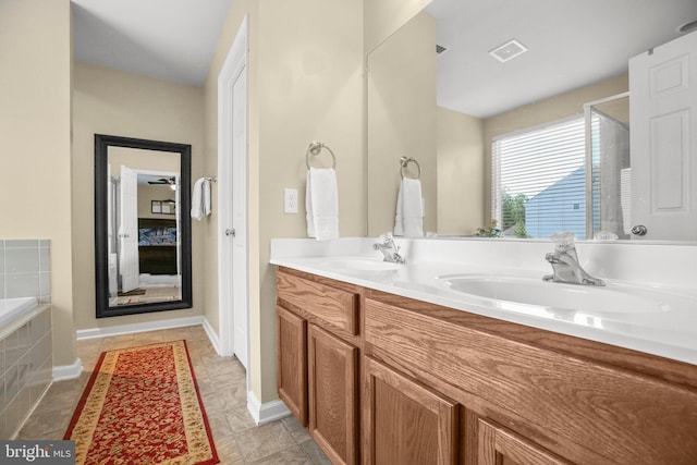 bathroom with tiled bath, double vanity, baseboards, and tile patterned floors