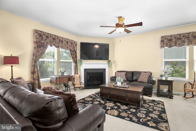 carpeted living area with ceiling fan, a glass covered fireplace, and baseboards