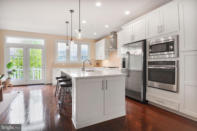 kitchen featuring stainless steel appliances, a sink, wall chimney range hood, dark wood-style flooring, and light countertops