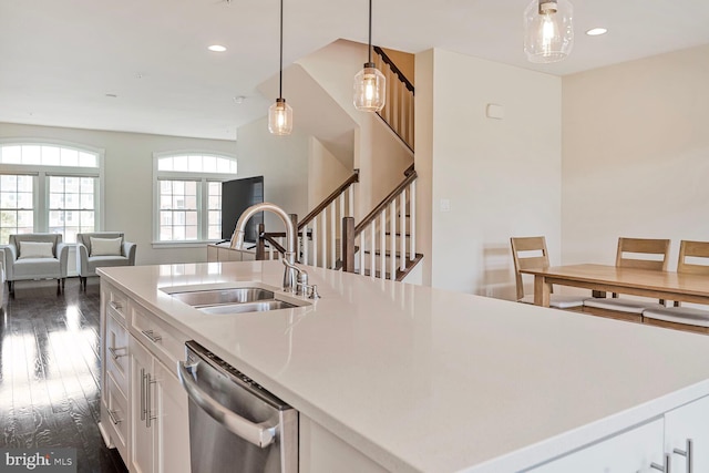 kitchen with stainless steel dishwasher, a sink, open floor plan, dark wood-style floors, and white cabinetry