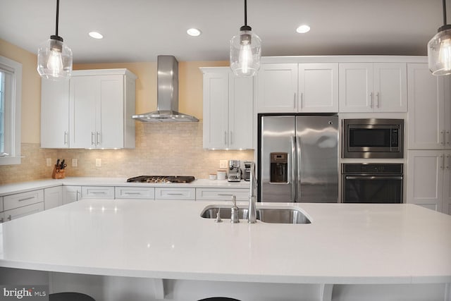 kitchen featuring appliances with stainless steel finishes, wall chimney exhaust hood, a sink, light countertops, and a kitchen island with sink