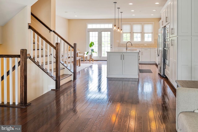 kitchen with dark wood finished floors, a sink, freestanding refrigerator, an island with sink, and white cabinets