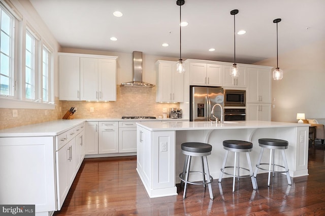 kitchen featuring appliances with stainless steel finishes, wall chimney range hood, backsplash, light countertops, and dark wood-style flooring