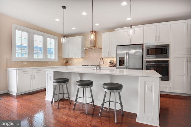 kitchen with appliances with stainless steel finishes, a sink, wall chimney range hood, white cabinets, and a breakfast bar area