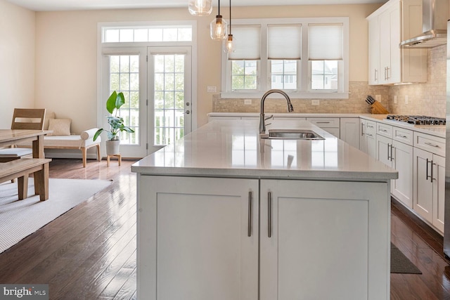 kitchen with wall chimney exhaust hood, a sink, stainless steel gas cooktop, backsplash, and dark wood finished floors