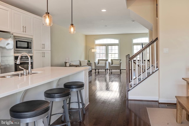 kitchen with stainless steel appliances, a sink, dark wood-style floors, white cabinets, and a kitchen bar
