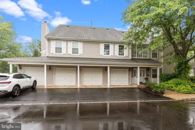 view of property with asphalt driveway, a chimney, a garage, and a shingled roof