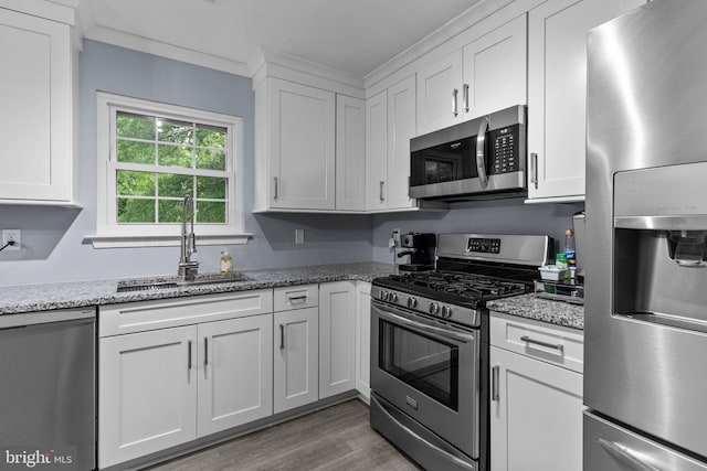 kitchen with stainless steel appliances, a sink, white cabinets, wood finished floors, and light stone counters