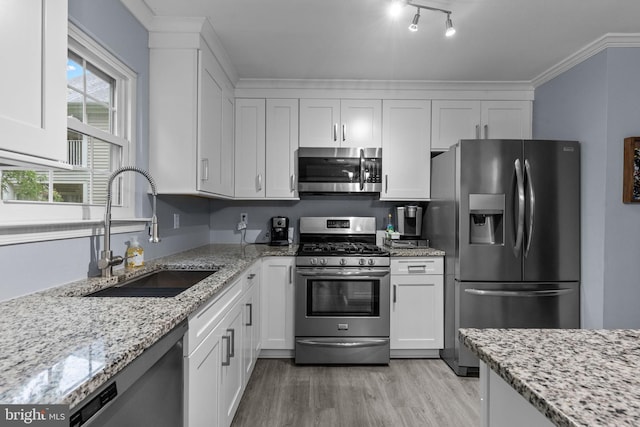 kitchen featuring stainless steel appliances, a sink, light wood-style flooring, white cabinets, and light stone counters