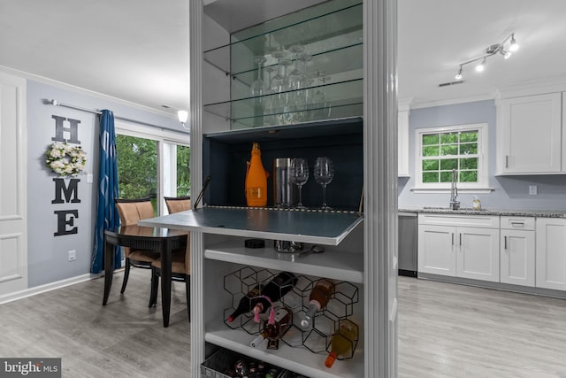 kitchen featuring a sink, crown molding, dishwasher, light wood finished floors, and white cabinetry