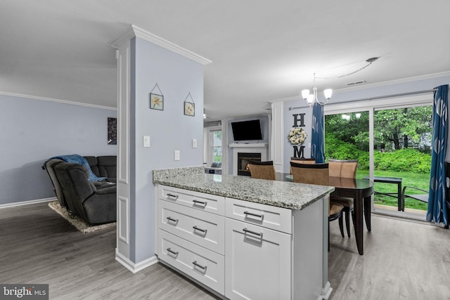 kitchen with open floor plan, light wood finished floors, white cabinetry, light stone counters, and crown molding